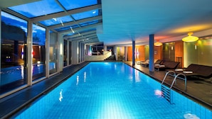 Ein Innenpool mit Glaswänden, Liegestühlen und einer Treppe zu einer erhöhten Ebene.