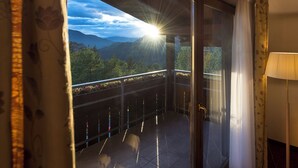 Ein Balkon mit Blick auf Berge und Bäume, eine Couch mit Kissen und eine Lampe.