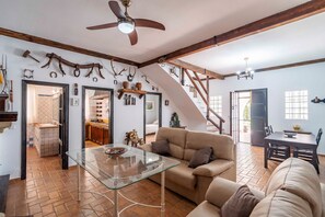 A spacious living area with a glass coffee table, a sofa, and a ceiling fan. A staircase leads to an upper level.