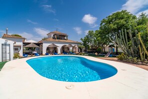 A swimming pool with lounge chairs, a building with a tiled roof, and cacti.