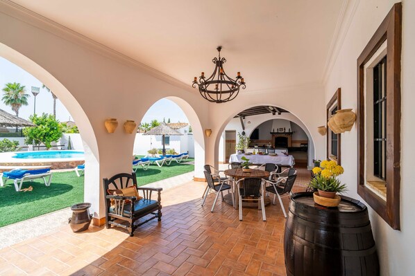 An outdoor patio with a table and chairs, a large barrel, and a view of a pool and lounge area.