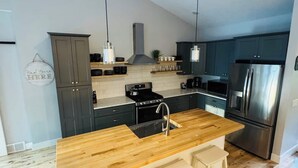 Une cuisine moderne avec un îlot central en bois, des appareils électroménagers en acier inoxydable et des meubles de rangement aux couleurs sombres.
