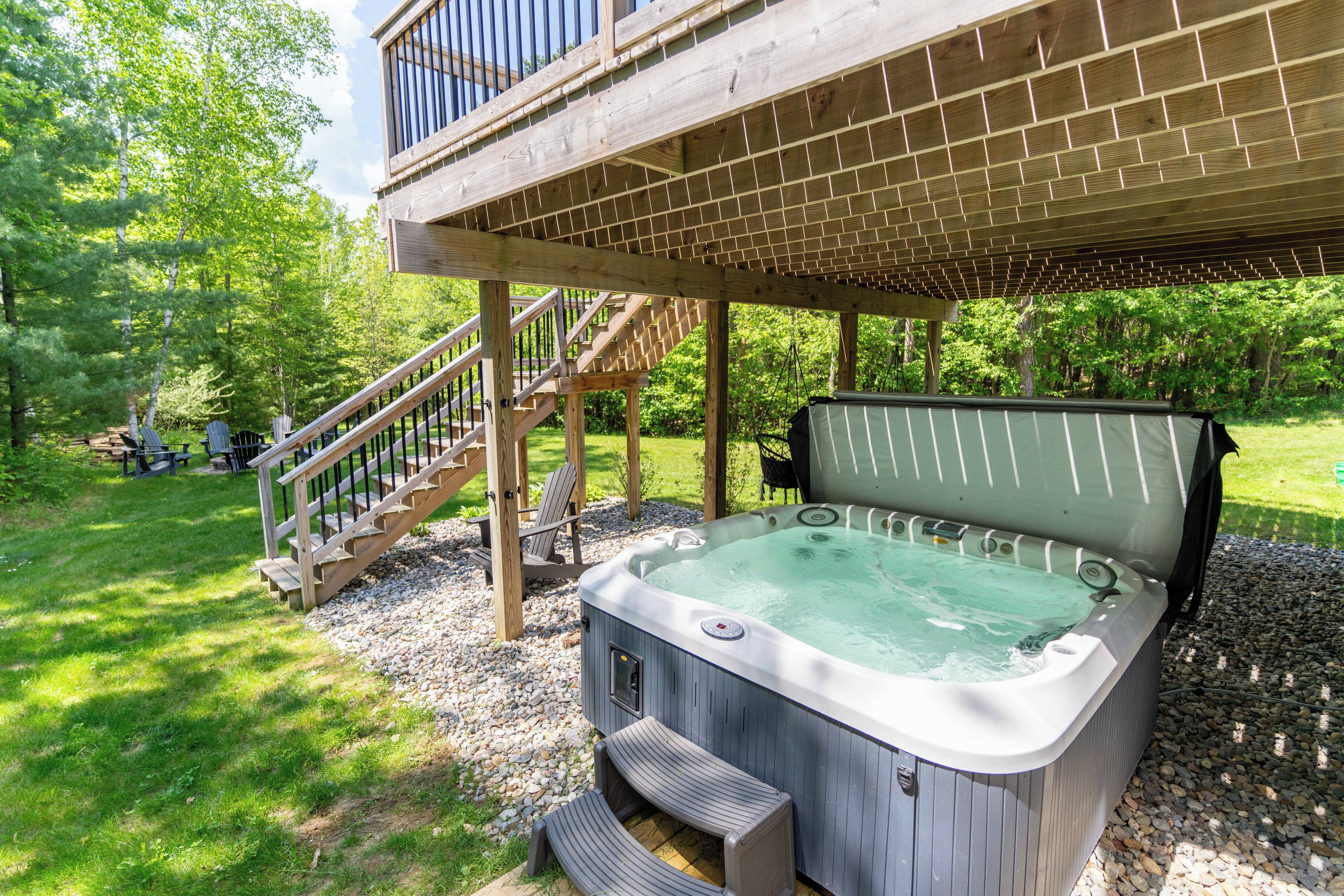 Un bain à remous installé sous une terrasse en bois, accessible par un escalier menant à un niveau supérieur, le tout entouré de verdure.