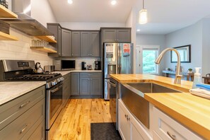Une cuisine moderne avec des meubles gris, des appareils en acier inoxydable et un plan de travail en bois.