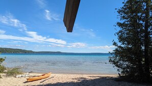 Una playa con una estructura de madera sobre ella, una canoa en la arena y un árbol grande a la derecha.