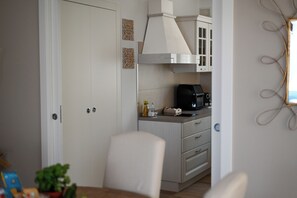 Ett kompakt kök med en vit dörr, en rostfri köksfläkt, en kaffebryggare och en liten arbetsbänk.