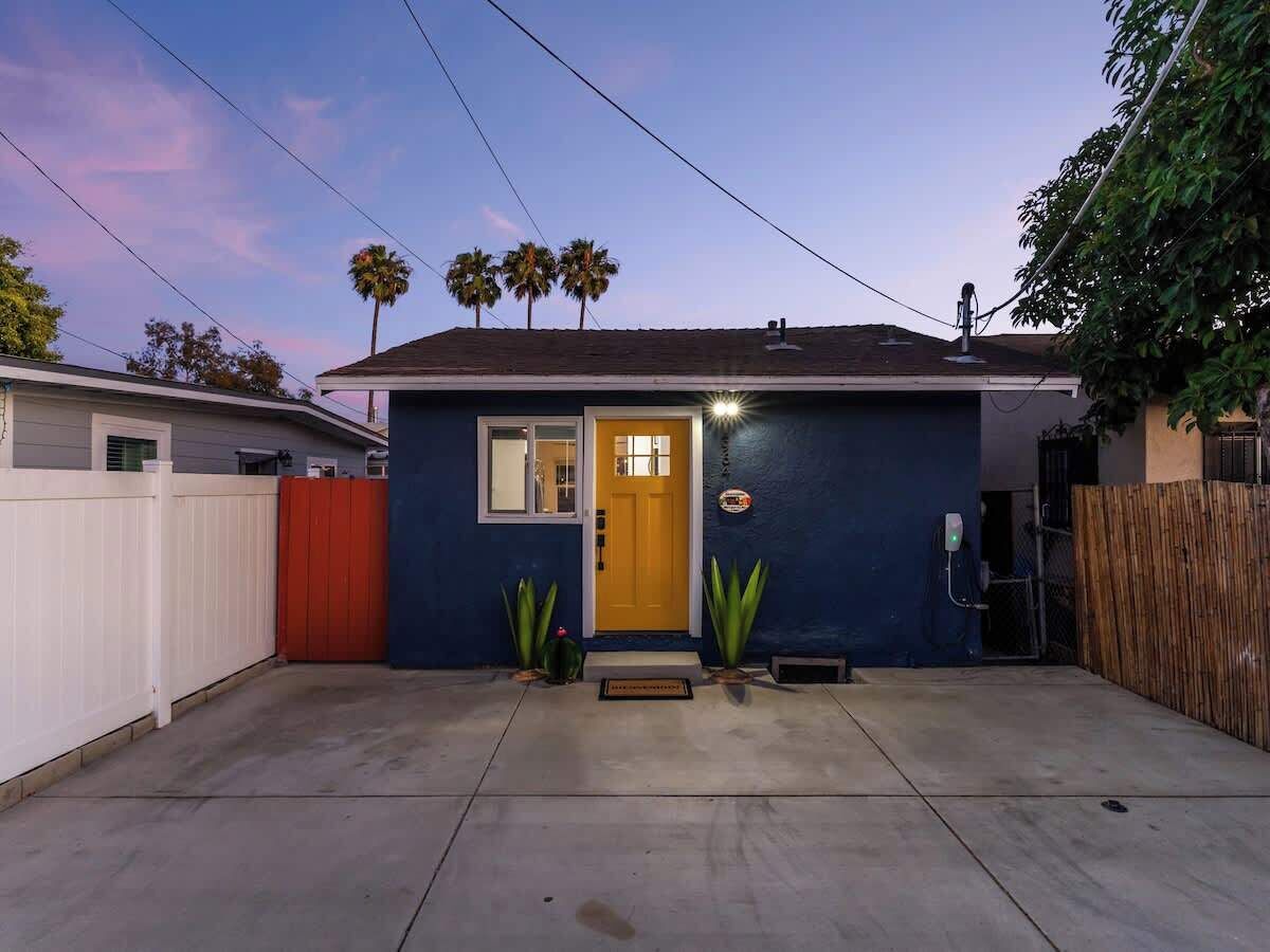 A single-story house with a yellow front door, a small porch, and a red gate.