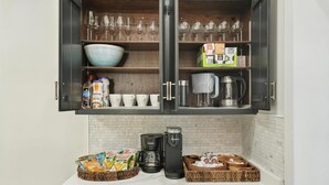 A kitchen with a cabinet containing glassware, bowls, coffee makers, and kitchen utensils. - Golden Dunes Stay Valpo | 5 BR, 3 King Beds | Game Area + Fire Pit + Deck Lounge (Valparaiso)