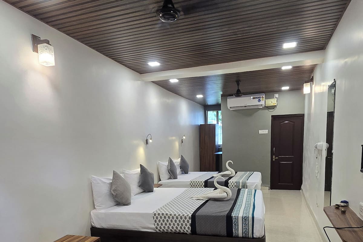 Una habitación de hotel moderna con dos camas, un banco de madera, una mesita y un pasillo que lleva a una puerta.