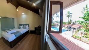 A bedroom with a bed, bedside table, and a view of a swimming pool and palm trees.
