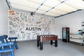 Une pièce avec un baby-foot, une chaise bleue et une fresque murale représentant divers gribouillages et le mot « AUSTIN ».