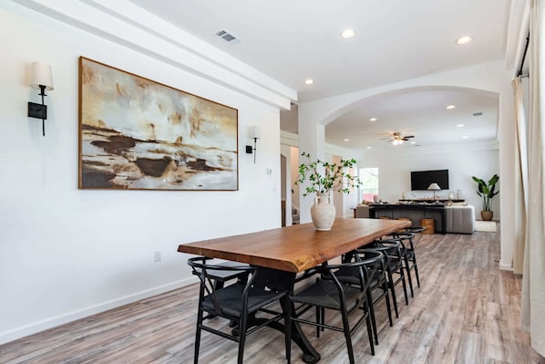 Un coin repas avec une table en bois, des chaises noires, un grand tableau abstrait et un vase avec une plante.
