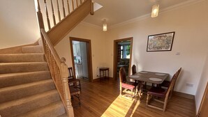 A spacious living area with a wooden staircase, a dining table with chairs, and a kitchen visible through an open door. - Shawsmill outside Hurlford (Hurlford)