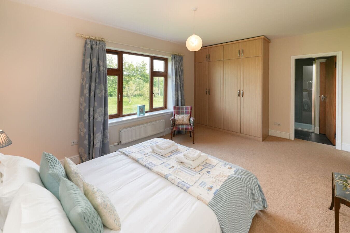 A bedroom with a bed, a chair, a wardrobe, and a window with curtains.