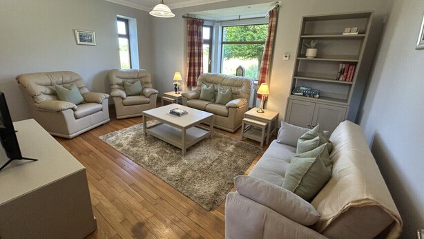 A living room with two sofas, a coffee table, and a TV stand. There is a bookshelf and a window with curtains. - Shawsmill outside Hurlford (Hurlford)