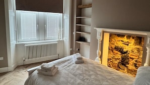 Een slaapkamer met een bed, een radiator, een raam met zonwering en een muur van steen.