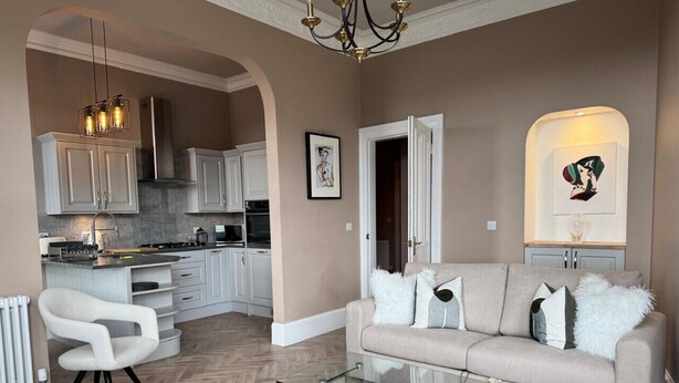 Een moderne woonkamer met een glazen salontafel, een beige bank en een witte fauteuil.