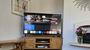 A flat-screen TV on a wooden stand with a remote control, a bench, and a fireplace with flowers.