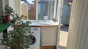 A compact kitchen with a washing machine, a green plant, and a window overlooking a backyard.