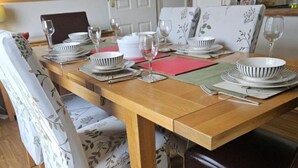 A dining table set with plates, bowls, and wine glasses, surrounded by upholstered chairs with floral patterns.