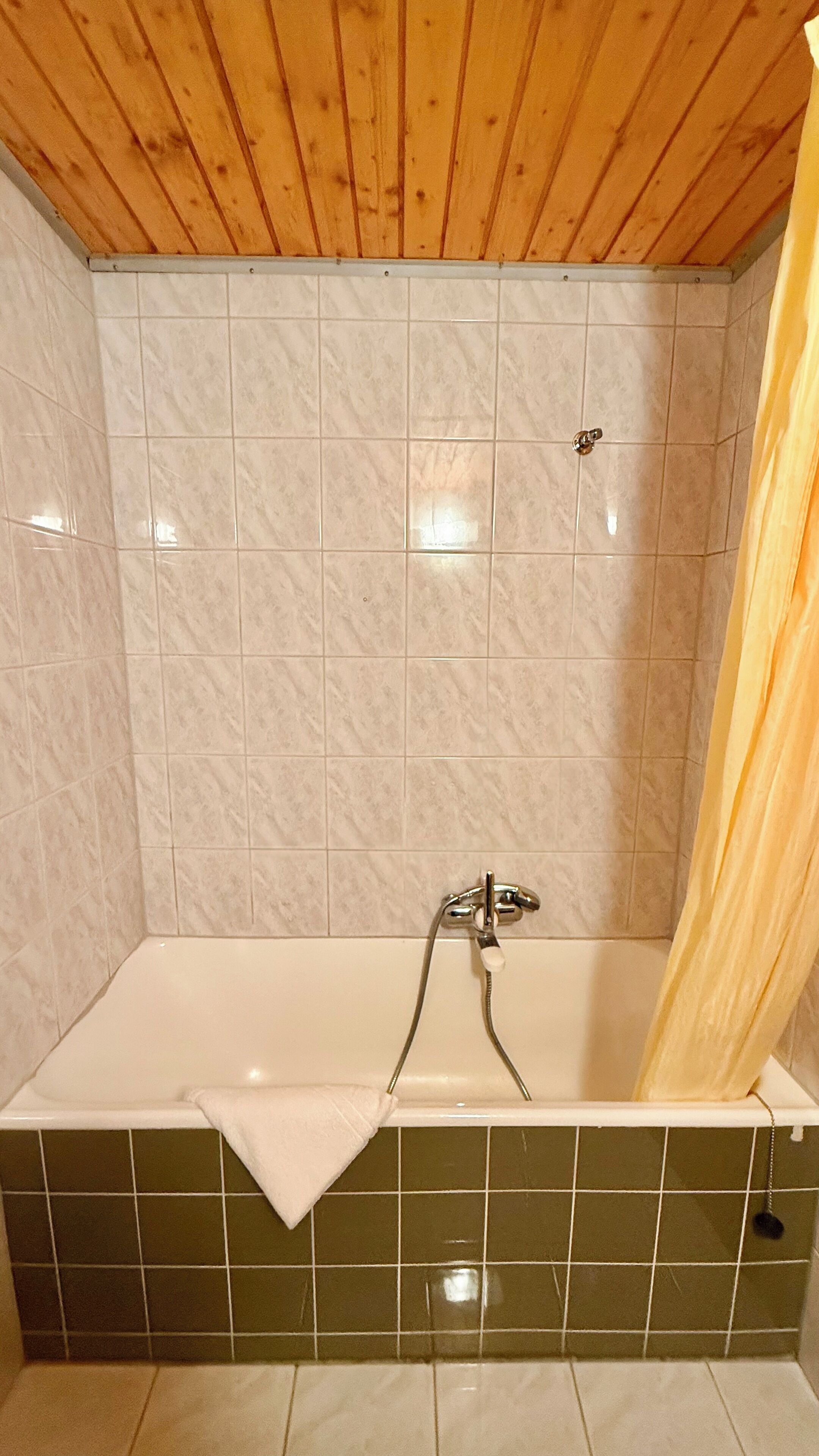 A bathroom with a wooden ceiling, a bathtub with a shower curtain, and tiled walls.