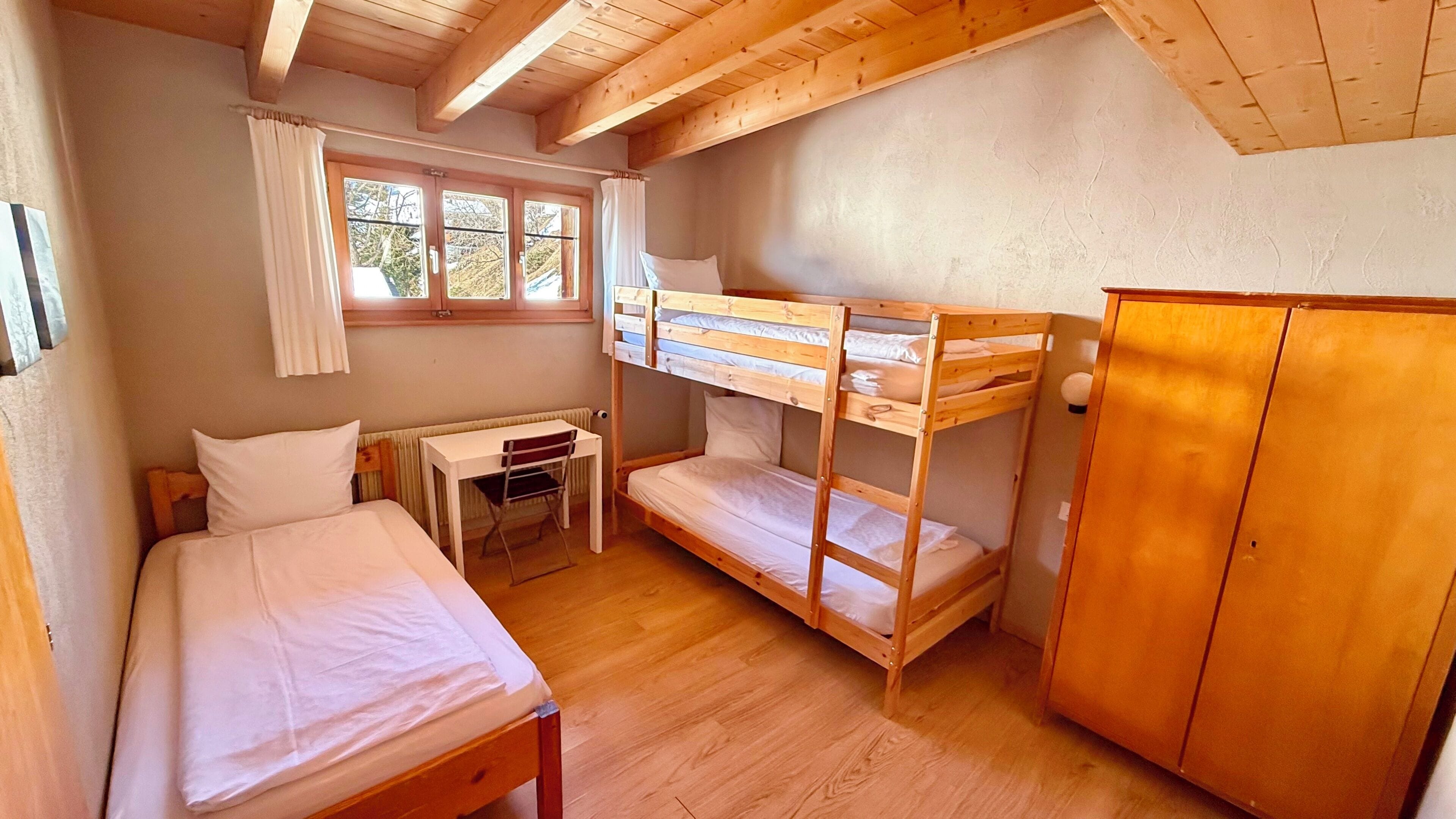 A bunk bed room with a desk and a wardrobe.