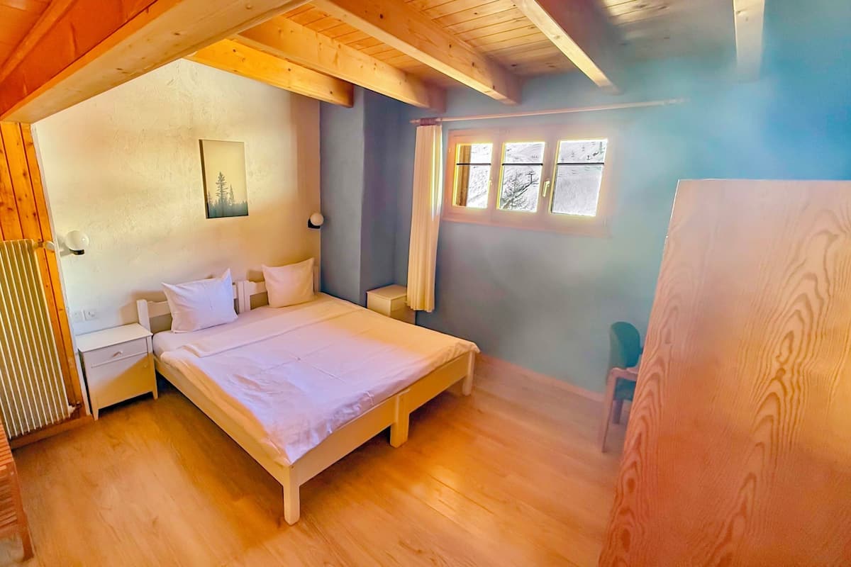 Un dormitorio con techo de madera, una cama, una mesita de noche, un radiador y una ventana con cortinas.