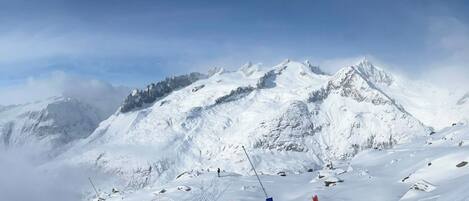 A snow-covered mountain slope with ski tracks and poles, indicating a ski resort.