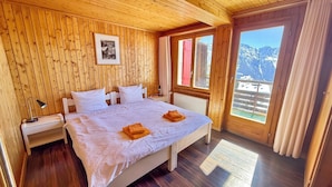 Una habitación con paneles de madera, una cama, una mesita de noche, una lámpara y un ventanal con vista a la montaña.