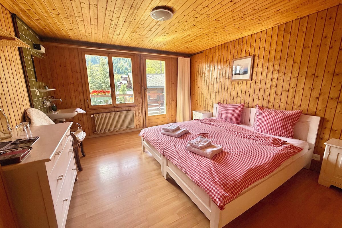Un dormitorio con paneles de madera, una cama, mesitas de noche y una ventana.
