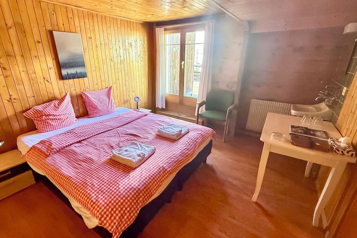 Una habitación de madera con una cama, una silla, una mesa con espejo y una ventana.