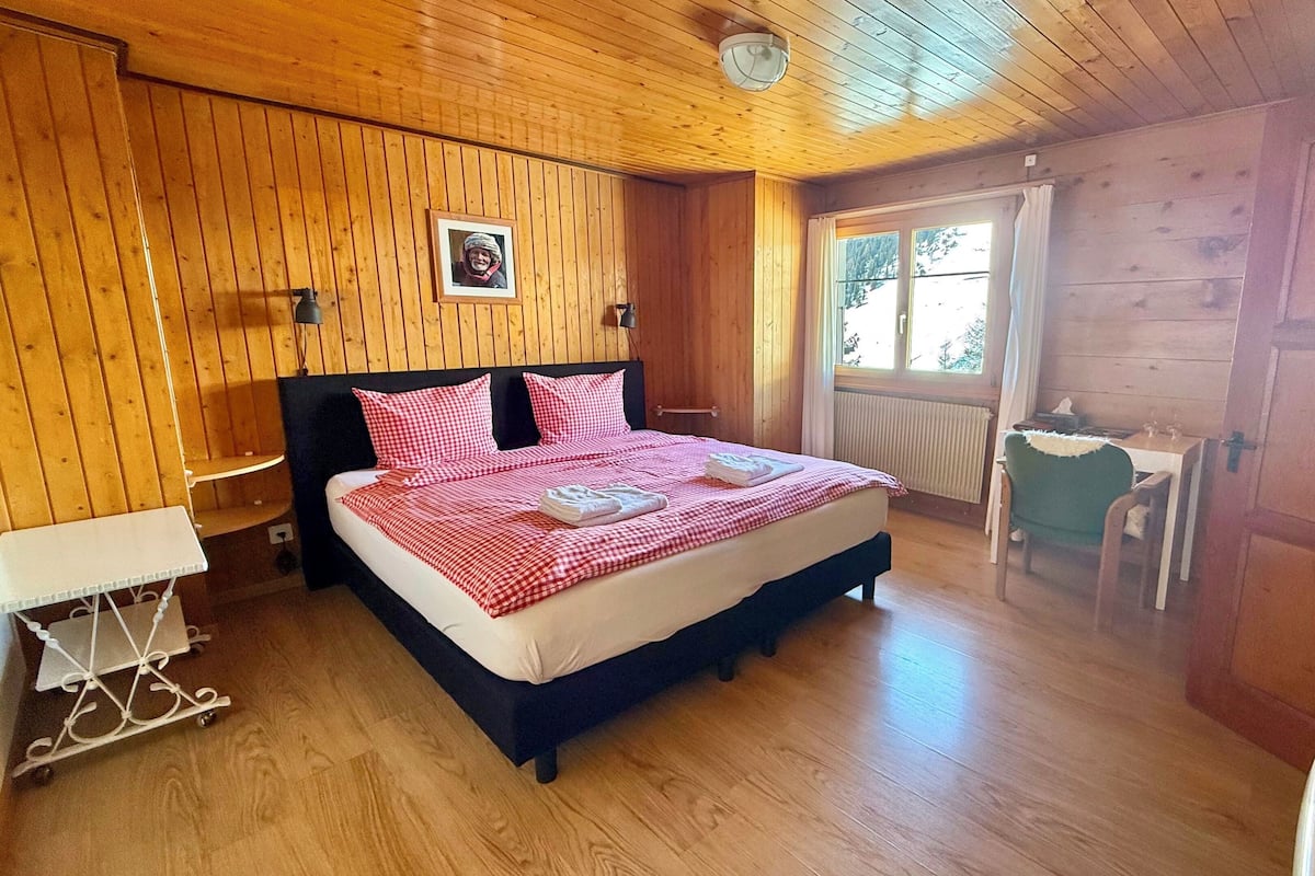 Un dormitorio con paneles de madera, una cama, una mesita de noche y un escritorio pequeño con una silla.