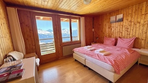Una habitación de madera con cama, una silla, una mesa y una ventana con vistas a la montaña.