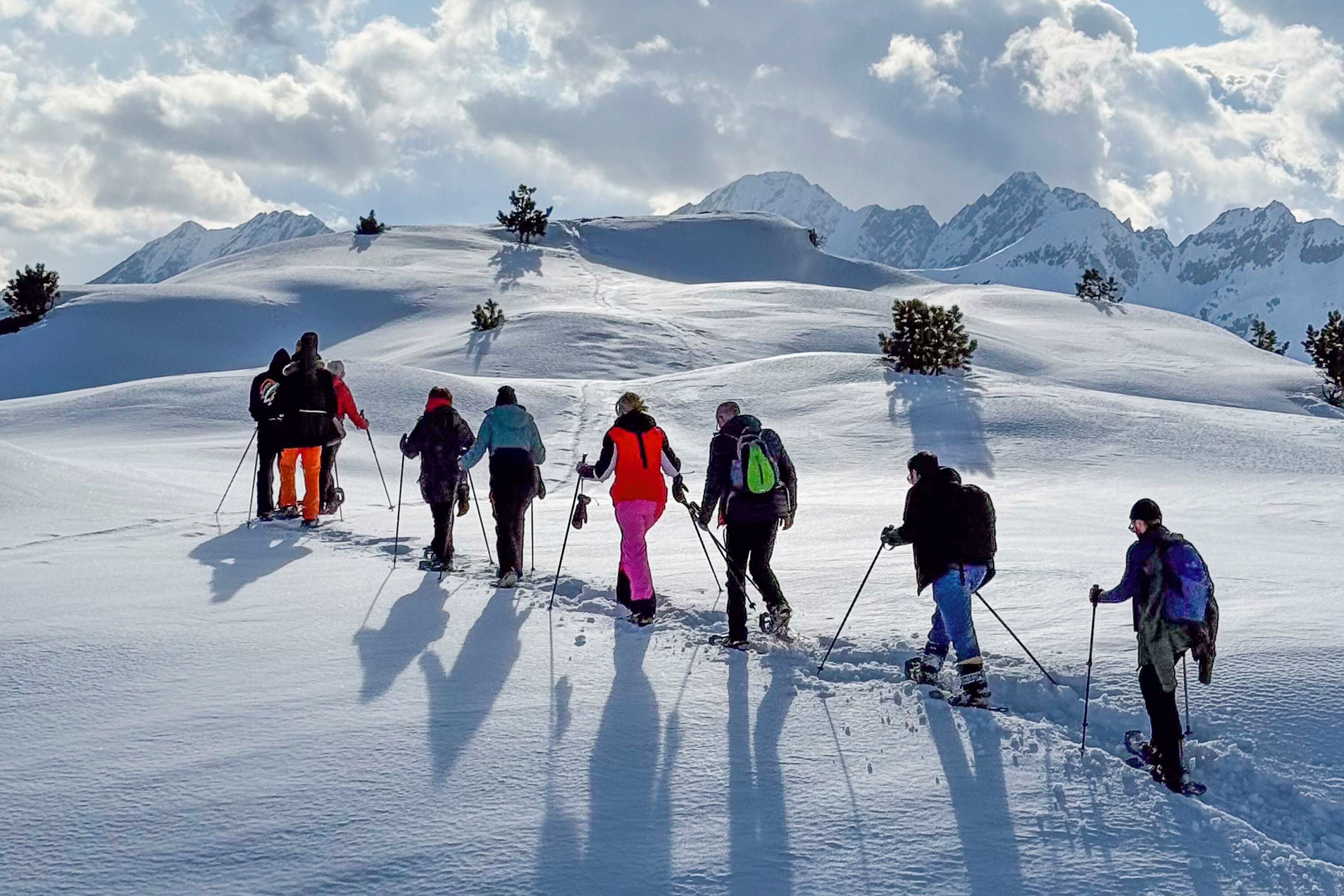 A group of people cross-country skiing on a snowy slope with mountains in the background.