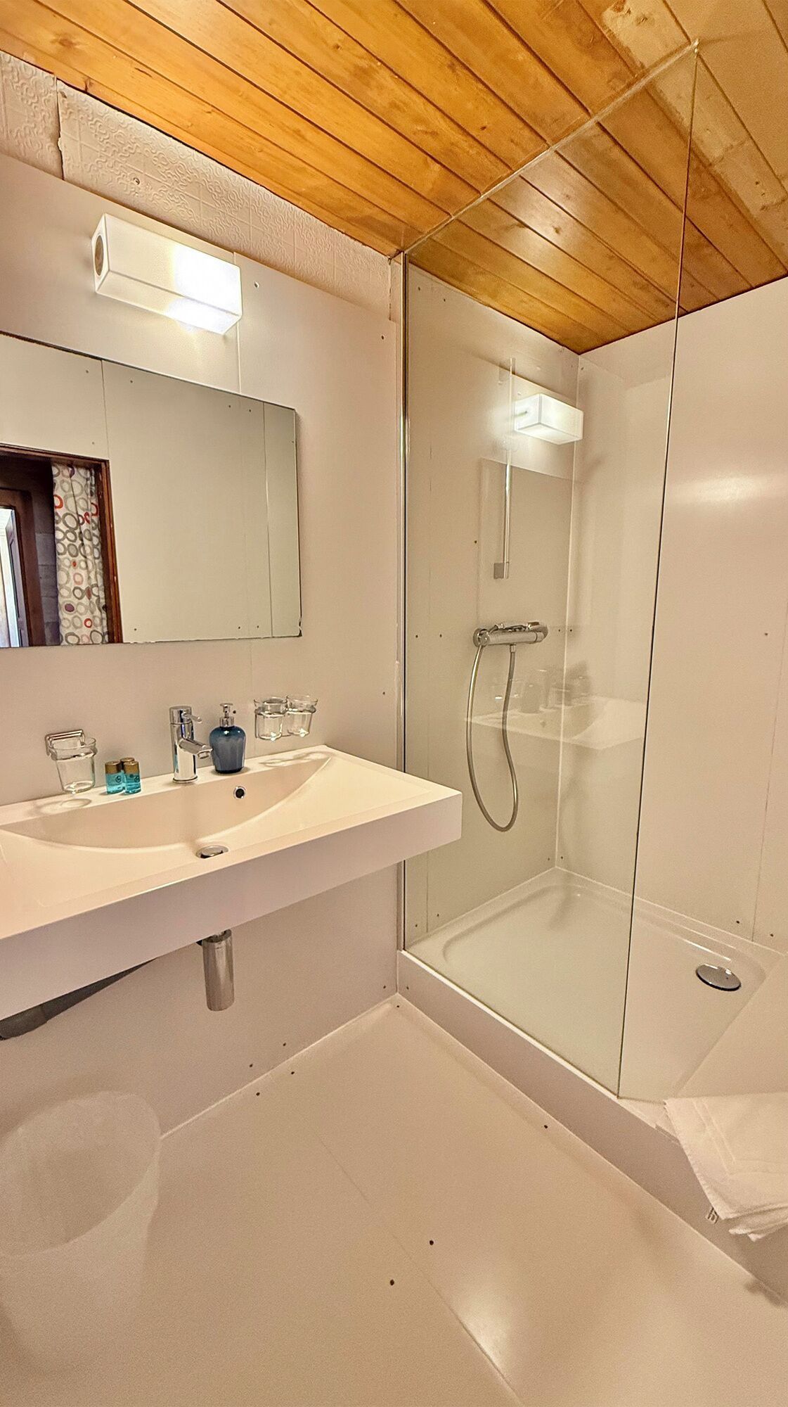 A modern bathroom with a white sink, mirror, and glass shower enclosure.