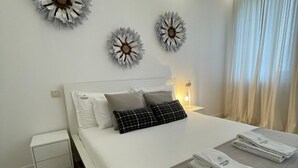A modern bedroom with a large bed, white nightstands, decorative wall art, and neatly folded towels on the bed.