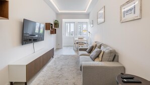 A modern living room with a TV, sofa, and a dining area with a table and chairs.