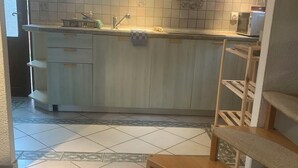 A kitchen with a central island, a sink, and a microwave. There is a clock on the wall and a window above the sink.