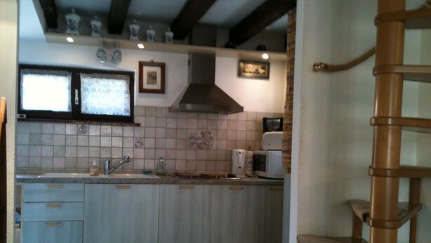 A kitchen with a large island, a built-in stove, and a microwave. There is a window above the sink and a wooden staircase to the right.