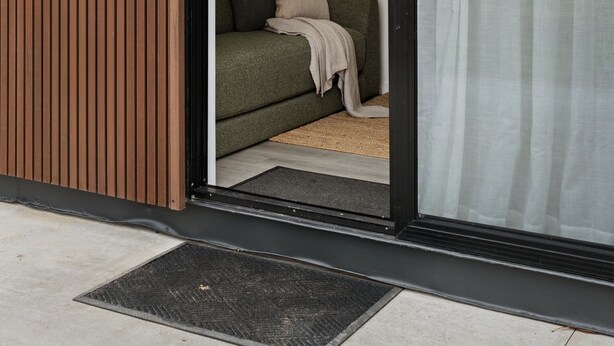 A modern building with a sliding glass door leading to a room with a green sofa and a beige throw blanket. - Hollow Mountain Cabin Laharum Dadswell bridge halls gap (Laharum)