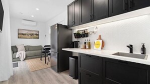 A modern kitchen with black cabinets, a white countertop, and a small dining area with a grey sofa and chairs. - Hollow Mountain Cabin Laharum Dadswell bridge halls gap (Laharum)