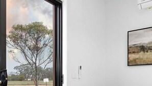 A living room with a sliding glass door leading to a backyard, a green sofa with a throw blanket, and a framed landscape painting on the wall. - Hollow Mountain Cabin Laharum Dadswell bridge halls gap (Laharum)