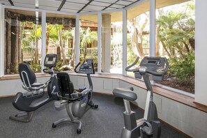 Un gimnasio con tres bicicletas estáticas, ventanas amplias y vistas al verdor exterior.