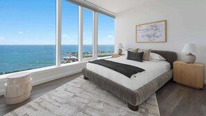A bedroom with a large window, a bed, bedside tables, and a view of the ocean.