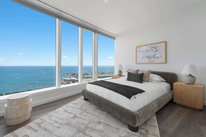 A bedroom with a large window, a bed, bedside tables, and a view of the ocean.