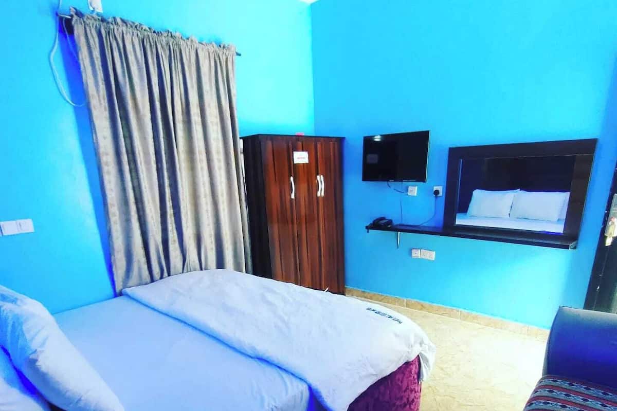A bedroom with a bed, a wardrobe, a TV, and a patterned sofa.