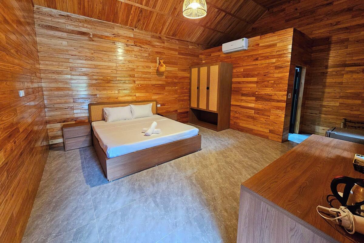 Ein Zimmer mit Holzboden, einem Bett, einem Schreibtisch und einer Hängelampe.