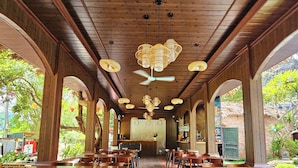 A spacious outdoor dining area with wooden tables and chairs, a central bar, and a ceiling fan. - An Riverside Ecolodge (Tay Hoa Lu)