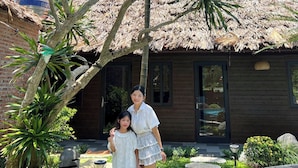 A wooden house with a thatched roof, surrounded by lush greenery and a swimming pool. - An Riverside Ecolodge (Tay Hoa Lu)