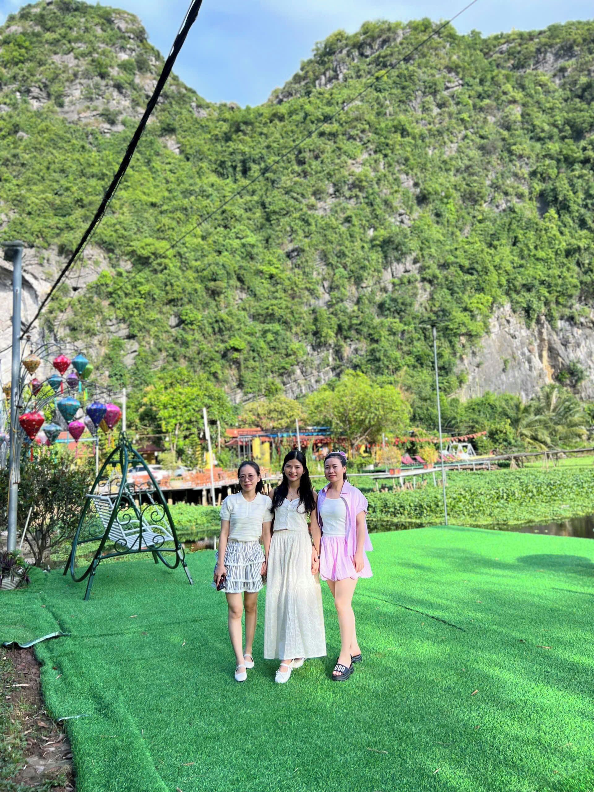 Three individuals standing on a green lawn with a mountainous backdrop.